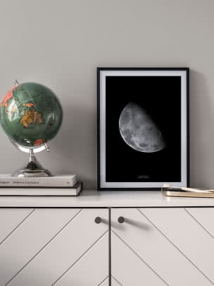 Framed moon print on a sideboard beside a globe and books