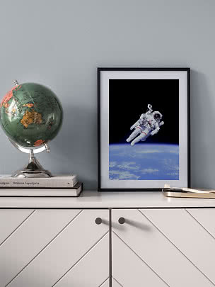 Framed astronaut poster above Earth on a white cabinet beside a globe.