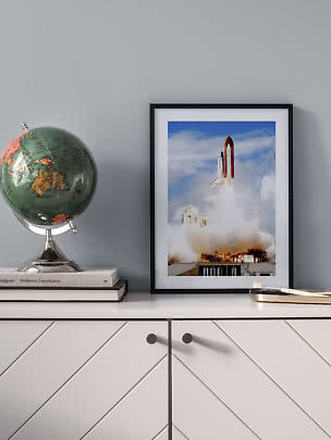Affiche encadrée d’une navette spatiale au décollage sur un meuble, à côté d’un globe vert