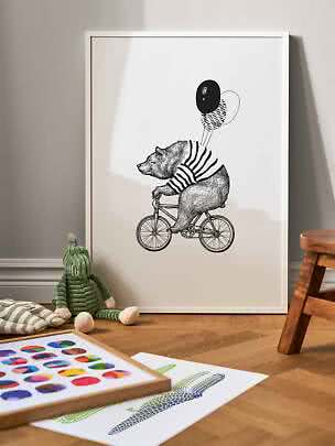 Indrammet sort-hvid plakat af en bjørn på cykel med balloner, lænet op ad væggen i et børneværelse