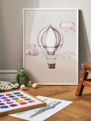 Poster per bambini incorniciato con mongolfiera rosa e nuvole, appoggiato al muro sul pavimento