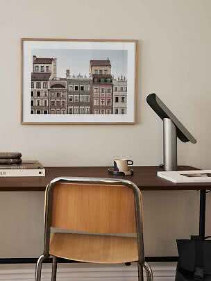 Gerahmter Stadtprint mit bunten Fassaden über einem Schreibtisch mit Stuhl und Lampe