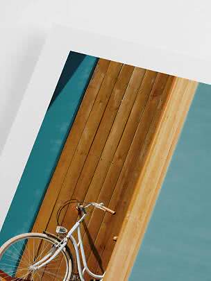 Vélo de ville blanc appuyé contre un mur en bois aux panneaux turquoise et blancs