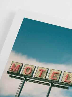Skråt foto af et motel-skilt med røde bogstaver mod blå himmel og hvide skyer