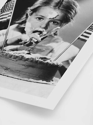 Black-and-white photo of a girl with frosting on her face beside a cake with American flags