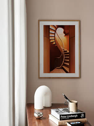 Framed art print of a curved wooden staircase above a desk with books and a mug