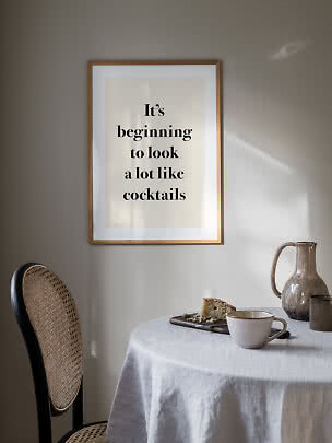 Framed typography poster above dining table with cup, pitcher and cake in soft sunlight
