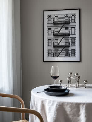 Spisehjørne med rundt bord, sorte tallerkener, vinglas og indrammet sort-hvid byfoto på væggen