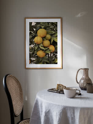 Poster incorniciato con arance su un ramo appeso sopra una tavola apparecchiata.