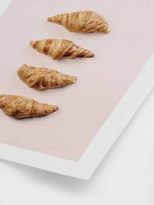 Vier Croissants auf einer hellrosa Fläche mit weißem Rand, von oben fotografiert.