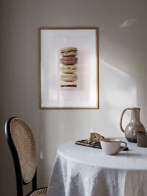 Indrammet plakat med fem macarons på væg over et bord med kop, kande og kage.