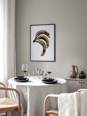 Ingelijste poster met drie gevlekte bananen op witte achtergrond boven een gedekte eettafel