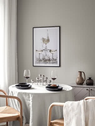 Angolo pranzo con tavolo rotondo, piatti neri, calici da vino e quadro incorniciato