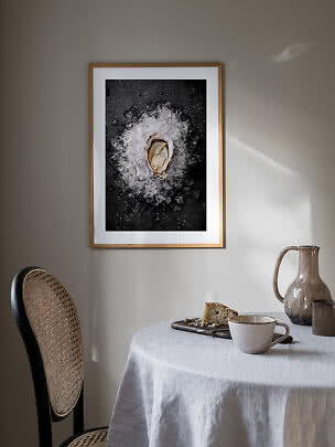 Framed art print of an oyster on crushed ice hanging above a laid dining table.