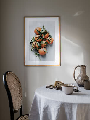 Affiche encadrée d’oranges et feuilles vertes sur mur clair au-dessus d’une table