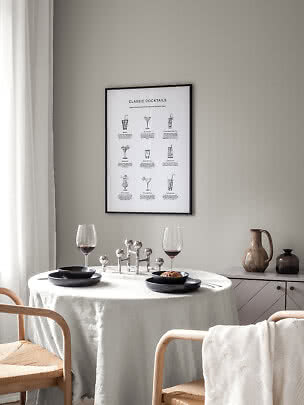 Essecke mit rundem Tisch, schwarzen Tellern, zwei Weingläsern und Cocktailposter an der Wand