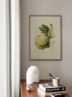 Framed botanical citrus print above a wooden table with books, vase and mug