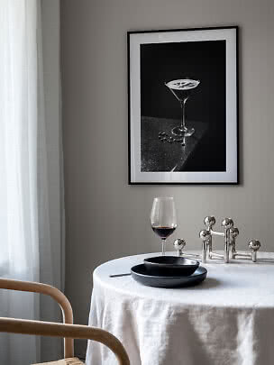 Angolo pranzo con tavolo rotondo, calice di vino e stampa cocktail in bianco e nero incorniciata