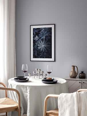 Dining area with round table, black plates, wine glasses and framed botanical print on a gray wall