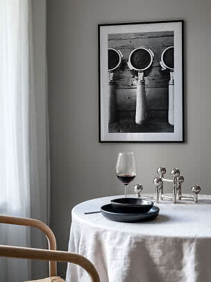 Tavolo da pranzo con tovaglia bianca, piatti neri, calice di vino e stampa in bianco e nero