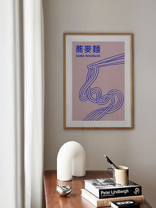 Indrammet soba noodles-plakat med blå linjetegning på lyserød baggrund over et træbord