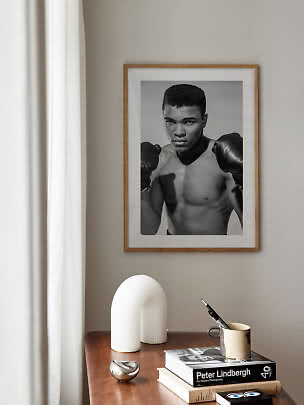 Poster incorniciato in bianco e nero di un pugile sopra un tavolo in legno con libri e oggetti déco