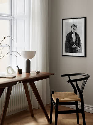 Minimalist workspace with wooden desk, black chair, table lamp, and framed black-and-white portrait.