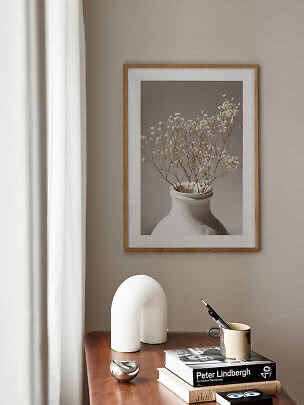 Stampa floreale incorniciata sopra comò in legno con libri, tazza e decori bianchi