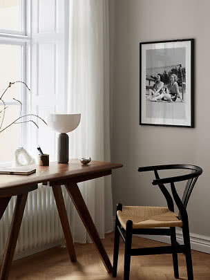 Espace de travail minimaliste avec bureau en bois, chaise noire, lampe et photo noir et blanc encadrée.