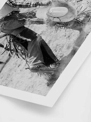 Schwarz-Weiß-Foto eines Cowboys auf bockendem Pferd mit Staub und fliegendem Hut