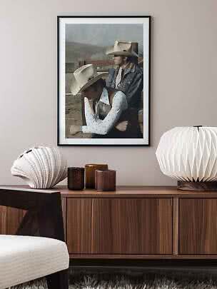 Poster incorniciato con due cowboy con cappelli chiari sopra una credenza in legno