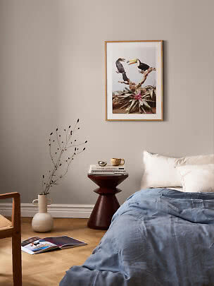 Chambre avec affiche encadrée de toucans au-dessus du lit, table d'appoint ronde et vase au sol