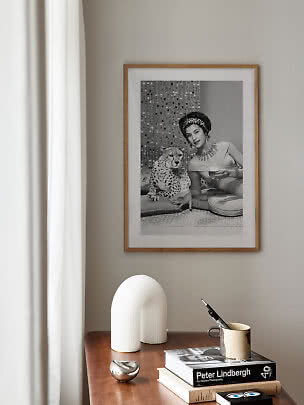 Ingelijste zwart-wit poster boven houten tafel met boeken, mok en witte sculptuurlamp