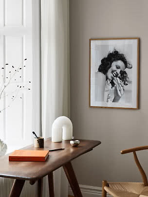 Holzschreibtisch am Fenster mit weißer Lampe und gerahmtem Schwarzweißfoto an der Wand