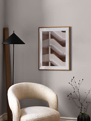 Soggiorno minimalista con poltrona color crema, lampada da terra nera e stampa incorniciata.