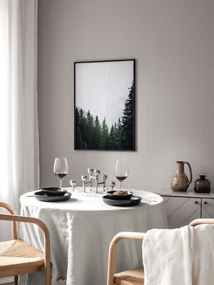 Dining nook with round table, black plates, wine glasses and forest wall art