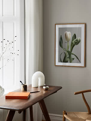 Stampa incorniciata con tulipani sopra un tavolo in legno in una stanza luminosa e minimalista.