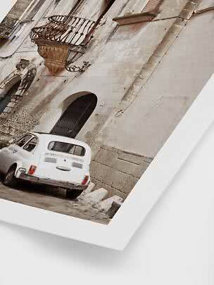 White vintage car parked beside an old stone building with a wrought-iron balcony.