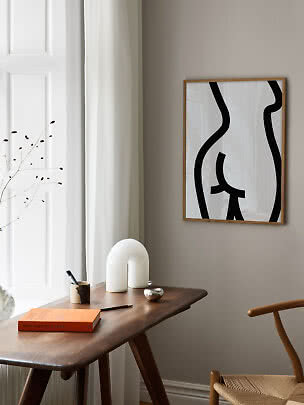 Abstract black and white poster in a light wood frame above a wooden desk in a bright minimalist room