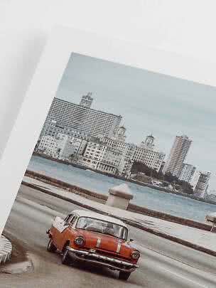 Framed photo of an orange vintage car on a coastal road with city and water behind