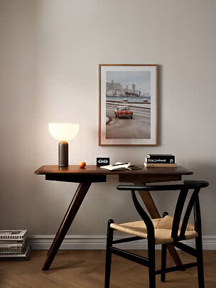 Dark wooden desk with lit table lamp, chair, and framed car photo on the wall