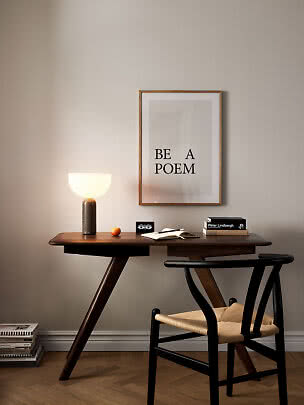 Scrivania in legno con lampada accesa, sedia e poster incorniciato su parete beige