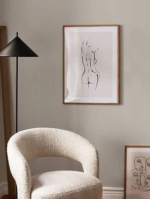 Bouclé armchair beside black floor lamp and framed line art on a beige wall