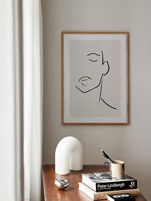 Disegno minimalista incorniciato di un volto sopra un tavolo in legno con libri, tazza e decori