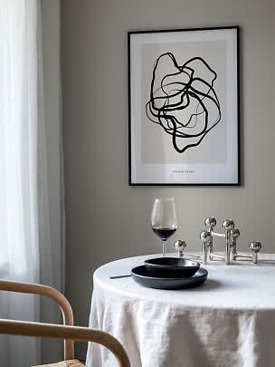 Gerahmtes abstraktes Schwarz-Weiß-Poster über einem Tisch mit weißer Decke, Weinglas und schwarzen Tellern