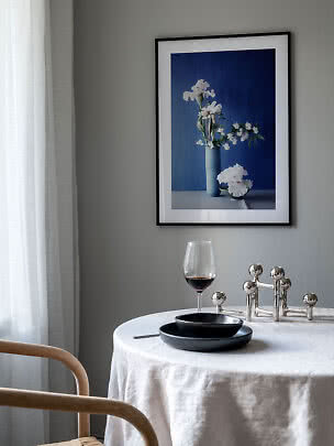 Essecke mit rundem Tisch, Weinglas und gerahmtem Blumenbild an grauer Wand