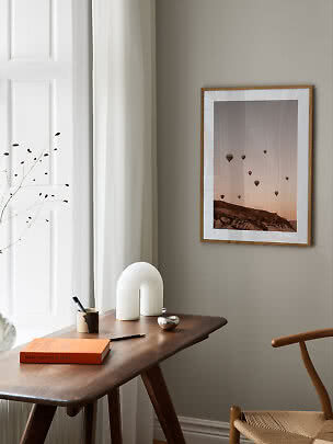 Gerahmter Heißluftballon-Print an beigefarbener Wand über einem Holzschreibtisch