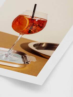 Cocktailglas met oranje drankje, ijsblokjes, rietje en sinaasappelschijf op metalen schaaltje