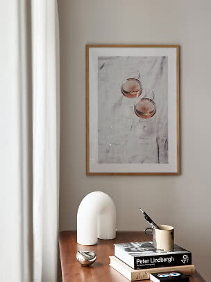 Gerahmtes Bild mit zwei Roséweingläsern auf Marmor über einer Holzkommode mit Büchern und Tasse