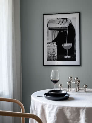 Angolo pranzo con tovaglia bianca, calice di vino e poster in bianco e nero di un cocktail